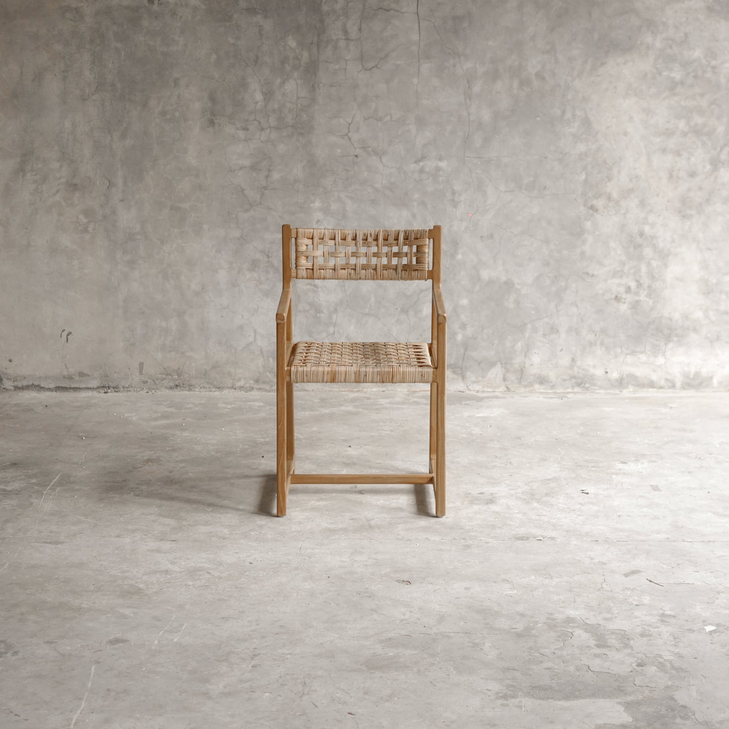 Wooden chair with woven seat and backrest against a gray concrete wall.