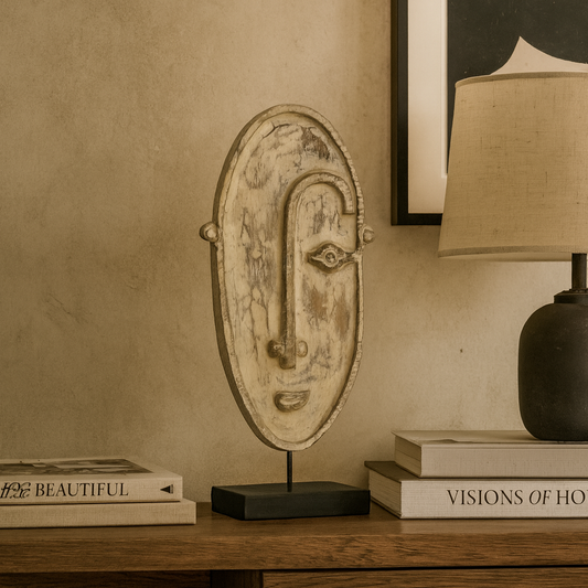 Decorative mask on a wooden surface with books and a lamp in the background