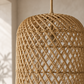 Close-up of a woven natural rattan pendant light in a warm tan color, hanging against a softly lit neutral wall.