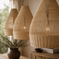 Three woven pendant lights hanging in a room with a plant and wooden surface.