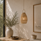 Nestled corner with a wooden table, woven basket pendant light, and framed artwork.