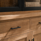 Wooden cabinet with black handles and glass door in the background