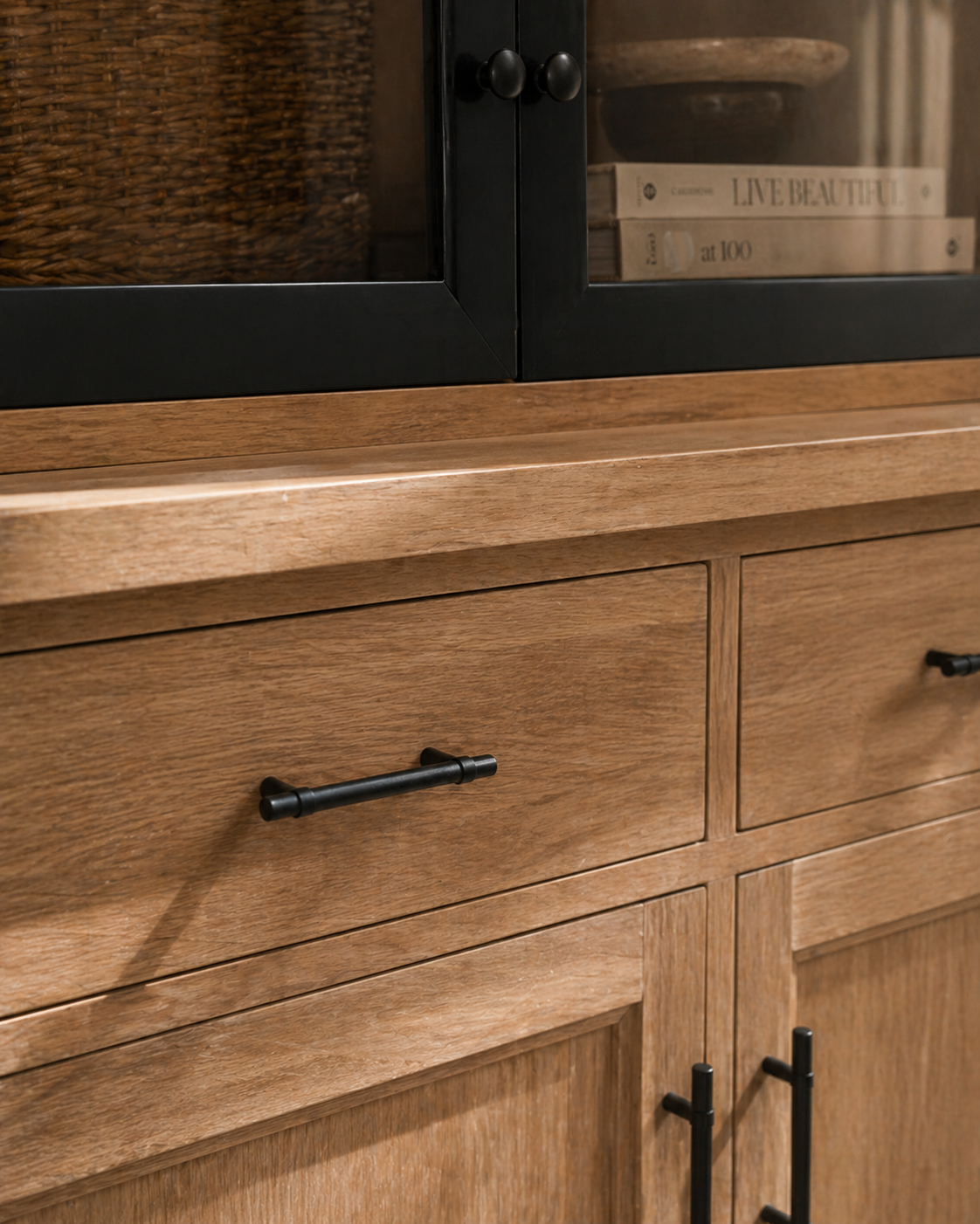 Wooden cabinet with black handles and glass door in the background