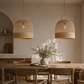 Dining room with wooden table, chairs, and wicker pendant lights.