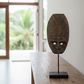 Wooden mask on a stand in a room with a window and plants outside