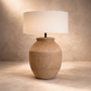 Table lamp with textured ceramic base and white shade on a neutral background