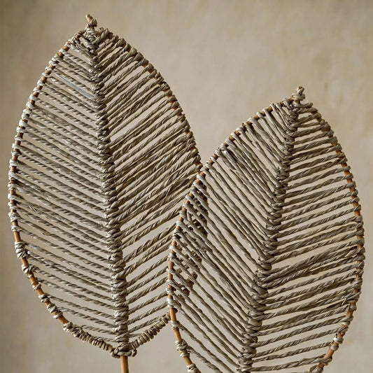 Two large woven leaf-shaped wall art pieces mounted on bamboo stakes, photographed against a neutral textured beige wall.