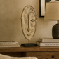 Decorative mask on a wooden surface with books and a lamp in the background