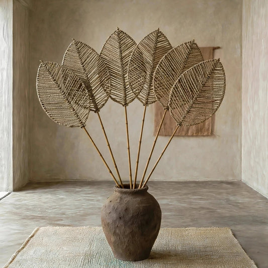 A decorative dried palm leaf arrangement in a rustic brown ceramic vase, placed on a woven rug inside a minimalist plaster room.