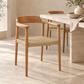 A modern wooden dining chair with a woven rope seat, positioned next to a stone table in a warm, minimalist dining room setting.