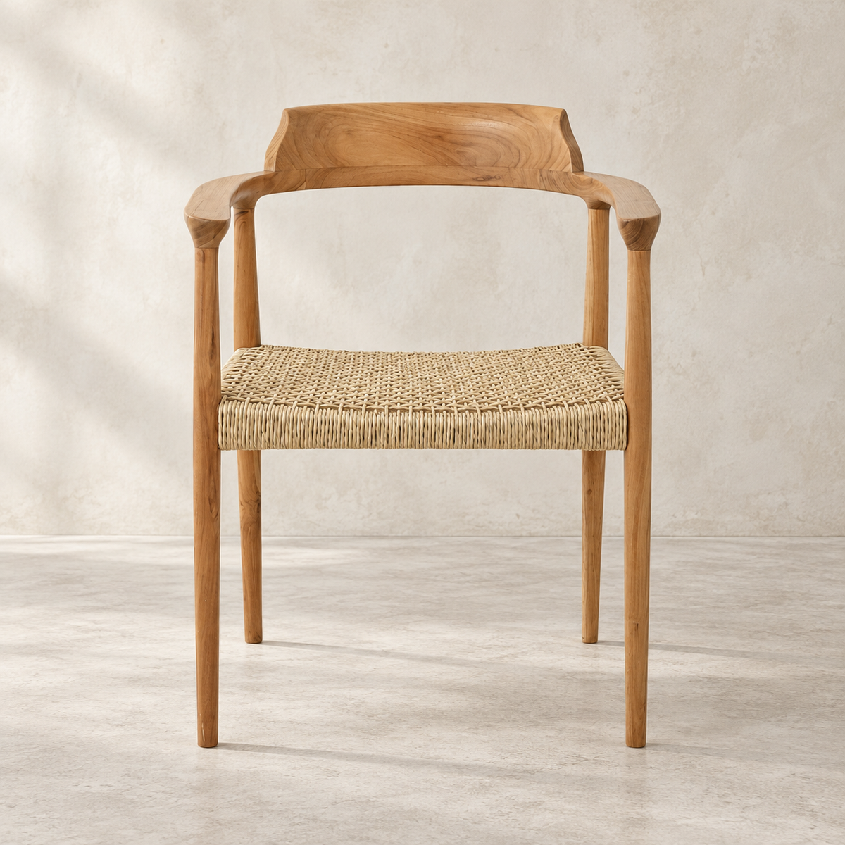 A mid-century modern wooden dining chair with a natural oak frame and a woven jute seat, shown against a textured light beige wall and concrete floor.