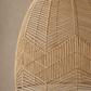 A close-up of a woven pendant light fixture made from natural tan wicker or rattan, showing the geometric openwork pattern against a warm beige wall.