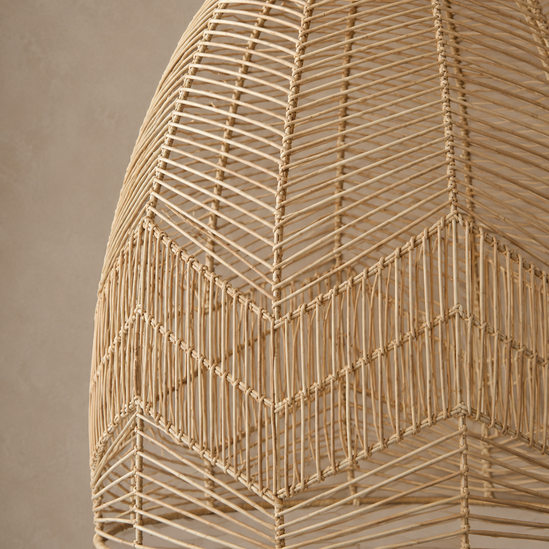A close-up of a woven pendant light fixture made from natural tan wicker or rattan, showing the geometric openwork pattern against a warm beige wall.