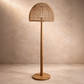 Wooden floor lamp with wicker shade against a beige wall.