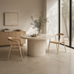 Round wooden dining table with two chairs in a modern interior setting.