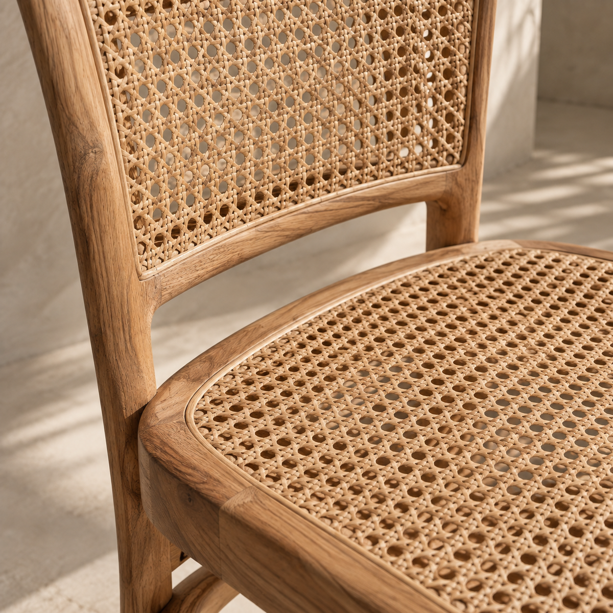 Close-up of a wooden dining chair with a woven cane backrest and seat, shown in warm natural light against a light neutral wall.