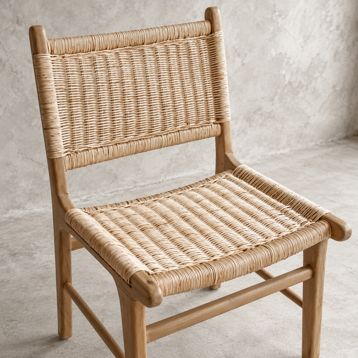 A wooden dining chair with woven natural rattan or seagrass on the seat and back, photographed in a minimalist studio setting with a textured concrete wall and floor.