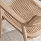 Close-up of a light natural wood armchair with a woven cane seat and back, shown on a textured gray floor.