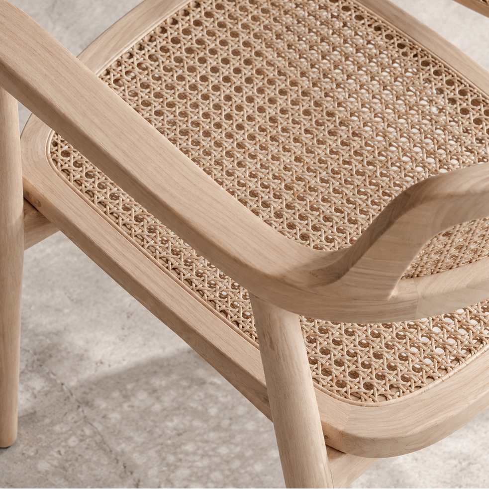 Close-up of a light natural wood armchair with a woven cane seat and back, shown on a textured gray floor.