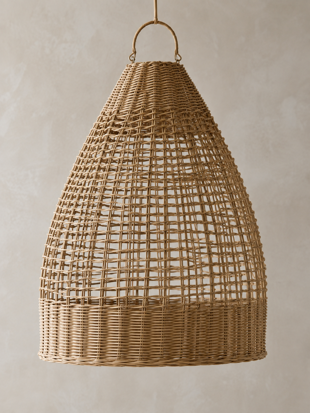 A teardrop-shaped woven rattan pendant light shade with a natural tan finish, suspended by a metal ring against a neutral textured beige wall.