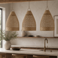 Three woven rattan pendant lights hang over a modern kitchen island with a stone countertop, brass faucet, and neutral-toned decor.