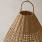 A close-up of a woven natural rattan basket with a rounded top and a single loop handle, set against a neutral light gray background.