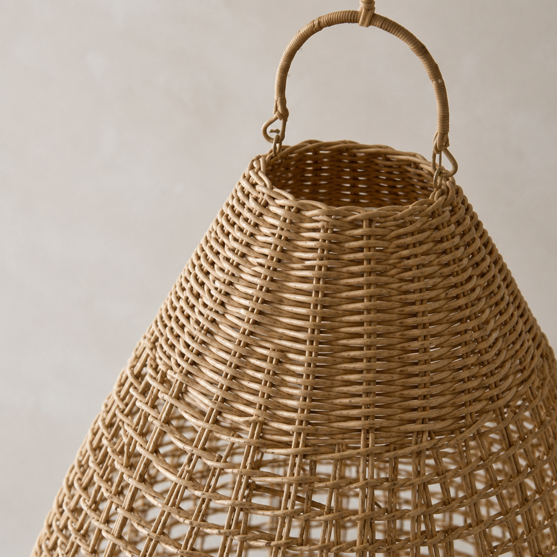 A close-up of a woven natural rattan basket with a rounded top and a single loop handle, set against a neutral light gray background.
