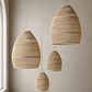 Three woven pendant light shades in different sizes hanging from thin cords in a minimalist room with a textured beige wall and floor.