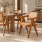 A mid-century modern wooden dining table and matching chairs with woven cane seats and backs, styled in a warm, sunlit dining room.