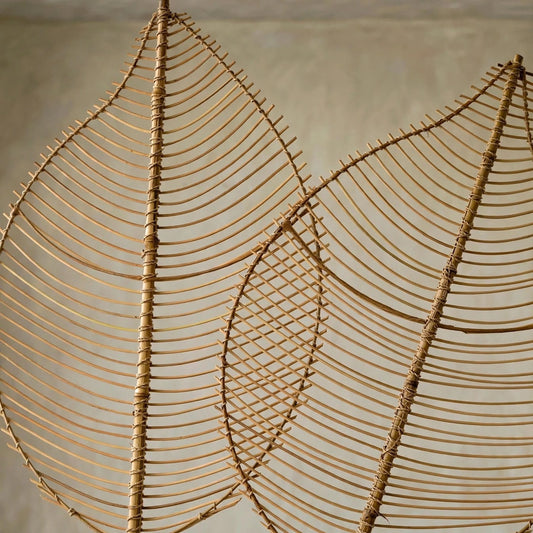 Two large woven leaf-shaped wall art pieces made from natural tan reed or bamboo, shown against a neutral textured wall.