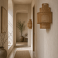 A warm, minimalist interior hallway with textured plaster walls, a woven runner rug, and two cylindrical woven wall sconces mounted on the right wall.
